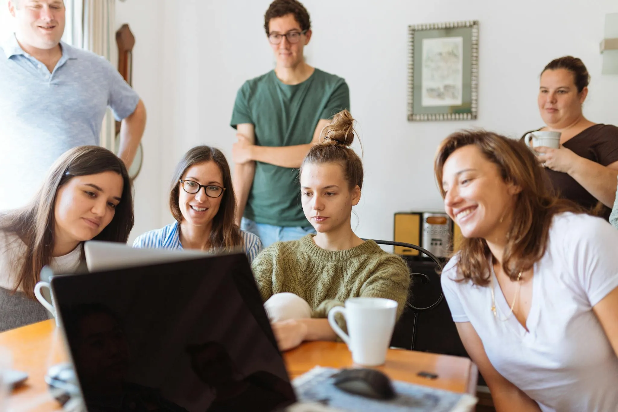 A group of colleagues gathered around a laptop, smiling